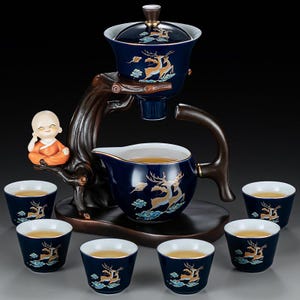 Könnte beinhalten: Komplettes Teeservice in Marineblau mit goldenen Hirsch- und Wolkenmotiven. Es umfasst eine Teekanne, Tassen und ein Serviergefäß, sowie einen Holzständer und eine kleine orangefarbene Figur. Die Tassen und die Teekanne sind mit Tee gefüllt.