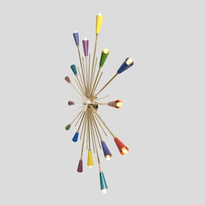 Könnte beinhalten: Eine moderne Mid-Century-Chandelier mit Messing-Finish und farbigen kegelförmigen Lichtern. Die Lichter sind in verschiedenen Farben, darunter Gelb, Grün, Blau und Rot. Die Leuchte hat mehrere Arme, die sich von einer zentralen Nabe aus erstrecken und ein Sternmuster bilden.