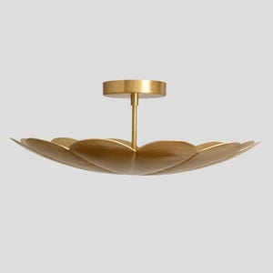 May include: A gold-colored ceiling light fixture with a petal-like design. The fixture has a central stem and a circular base for mounting. The light is made of metal and has a smooth, reflective surface. The overall shape is reminiscent of a flower.