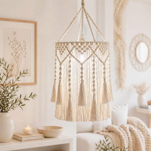 Puede incluir: Lámpara colgante de macramé color crema con diseño geométrico y borlas. La lámpara cuelga del techo y forma parte de un interior de estilo bohemio. Un elemento decorativo para la decoración del hogar.