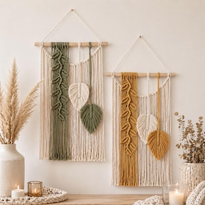 May include: Two macrame wall hangings with leaf designs. One in olive green and cream, the other in mustard yellow and cream. Each has a wooden dowel for hanging. Decorative home decor.