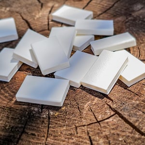 Peut inclure: Plusieurs carreaux rectangulaires blancs dispersés sur une surface en bois brun vieilli. Les carreaux sont de taille et de forme uniformes, avec une finition lisse et mate. L'image est bien éclairée, mettant en valeur la texture du bois et les lignes épurées des carreaux.