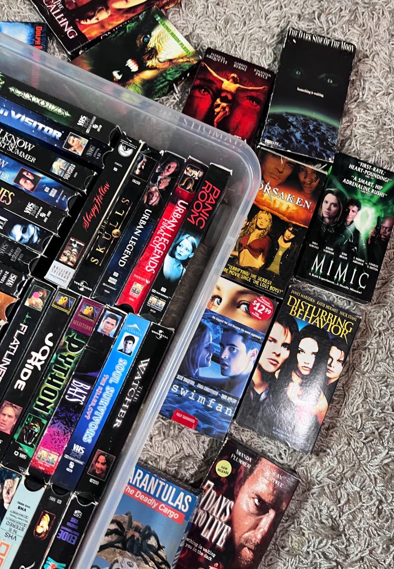 Może przedstawiać: Kolekcja r&oacute;żnych kaset VHS przechowywanych w przezroczystym plastikowym pojemniku, zawierająca tytuły takie jak The Dark Side of the Moon, Mimic, Disturbing Behavior, Swimfan, 7 Days to Live, Tarantulas, The Watcher, Soul Survivors, Bats, Python oraz Panic Room.
