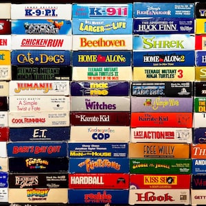 May include: A collection of fifty VHS movie tapes arranged in a grid, featuring titles such as Loch Ness, Chicken Run, Shrek, Home Alone, Jumanji, The Karate Kid, E.T., The Flintstones, Hook, and White Fang, with colourful spines and text.