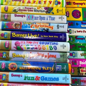 May include: A collection of Barney VHS tapes stacked horizontally and vertically. Titles include Barney's Rhyme Time Rhythm, Once Upon A Time, Night Before Christmas, Barney Live! In New York City, It's Time For Counting, Imagination Island, Halloween Party, and Fun & Games.