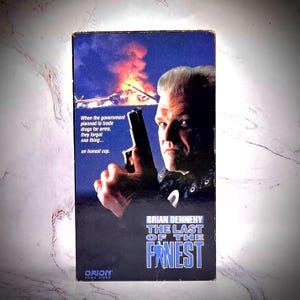 May include: A vintage VHS tape for the movie "The Last of the Finest" featuring Brian Dennehy. The cover has a dark blue background with a man holding a gun, and text that reads "When the government planned to trade drugs for arms, they forgot one thing... an honest cop."