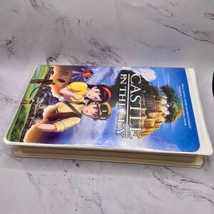May include: A VHS tape of the animated film "Castle in the Sky." The cover shows two animated characters against a blue sky and a floating castle. The title is clearly visible.