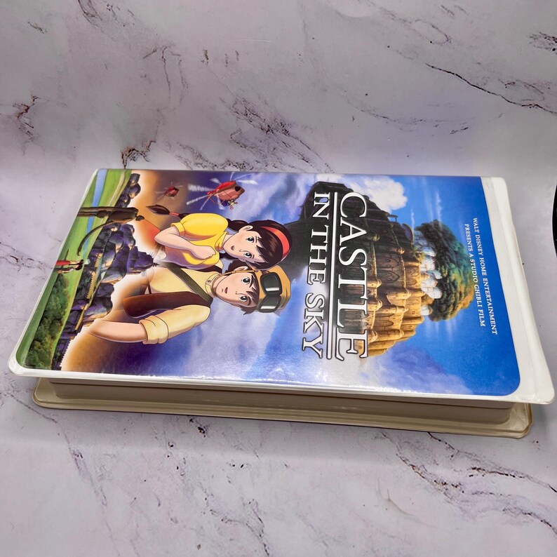 May include: A VHS tape of the animated film "Castle in the Sky." The cover shows two animated characters against a blue sky and a floating castle. The title is clearly visible.