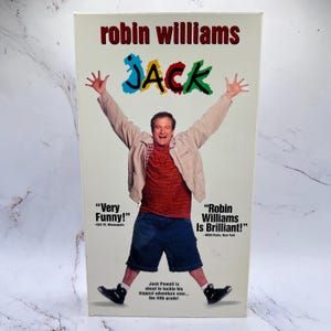 Puede incluir: Caja de VHS de la película "Jack" con Robin Williams. La imagen muestra a Williams con los brazos extendidos. El texto incluye el título de la película, el nombre del actor y citas.