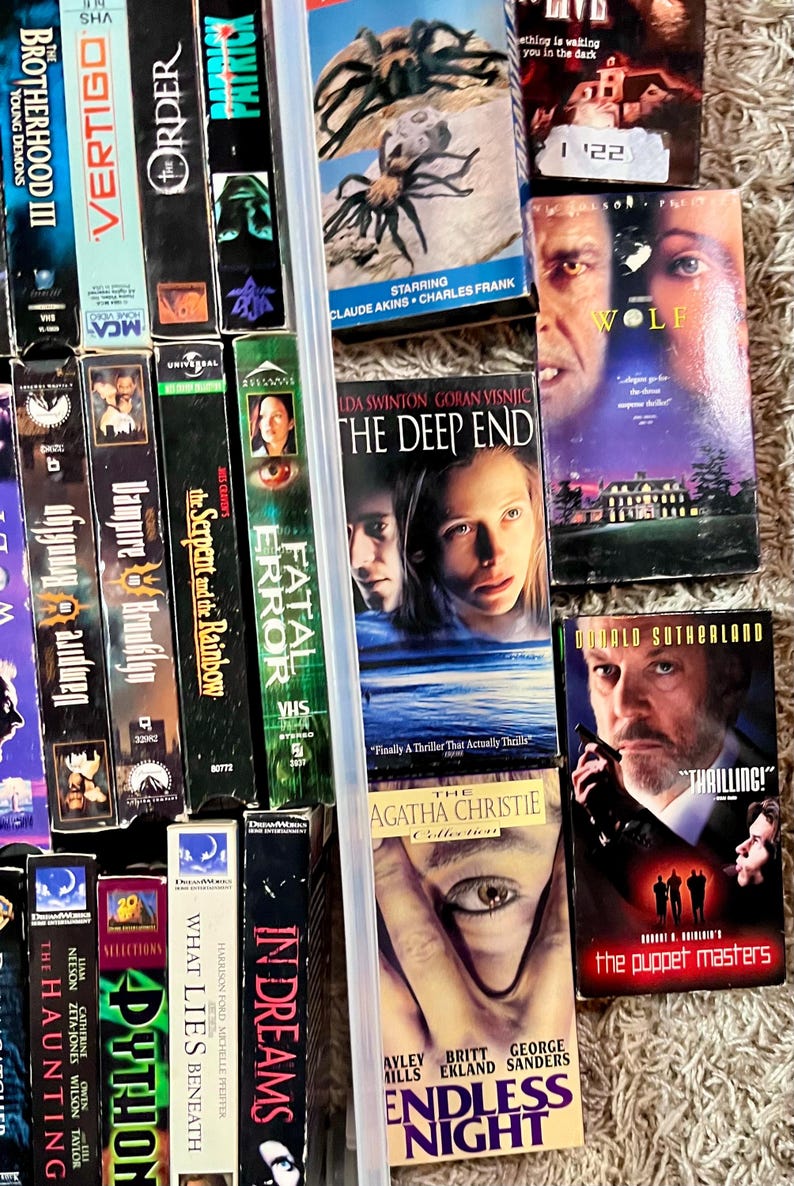 Może przedstawiać: Kolekcja r&oacute;żnych kaset wideo VHS z tytułami takimi jak The Brotherhood III, Vertigo, The Order, Patrick, The Deep End, Wolf, The Puppet Masters i Endless Night, pokazana z widocznymi grzbietami i przednimi okładkami.