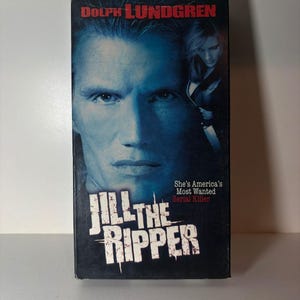 Może przedstawiać: Kaseta VHS z filmem Jill the Ripper z Dolphem Lundgrenem w roli gł&oacute;wnej. Okładka przedstawia duży, niebieskawy portret mężczyzny, mniejszy obraz kobiety trzymającej n&oacute;ż oraz tekst Jill the Ripper i She's America's Most Wanted Serial Killer.