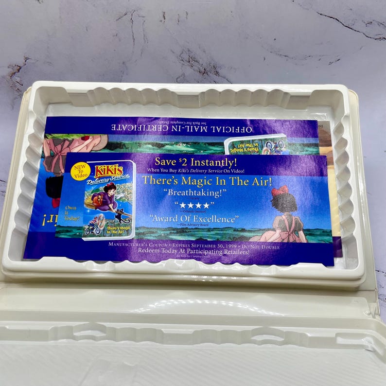 May include: A white plastic case holding promotional inserts for the animated film "Kiki's Delivery Service." The inserts include a coupon, a mail-in certificate, and a video cover with the film's title and characters.