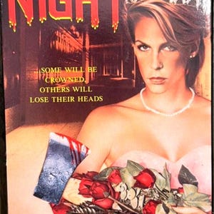 Może przedstawiać: Okładka kasety VHS filmu Prom Night przedstawiająca Jamie Lee Curtis w tiarze i r&oacute;żowej sukience, trzymającą bukiet czerwonych r&oacute;ż oraz zakrwawiony top&oacute;r. Tekst głosi: Jamie Lee Curtis, Prom Night, Some will be crowned, others will lose their heads.