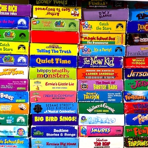 May include: A collection of colourful VHS tapes stacked in a grid, featuring titles such as Richie Rich, Dora the Explorer, The Muppet Caper, Sesame Street, The Magic School Bus, The Jetsons, The Flintstones, and Wallace & Gromit with various logos.