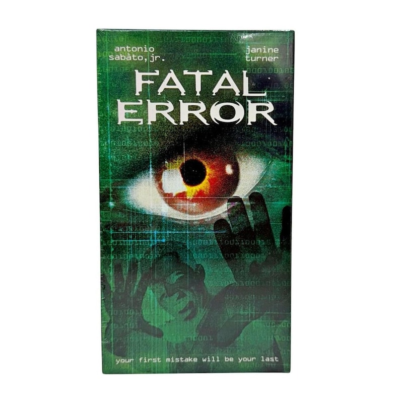 Może przedstawiać: Okładka kasety VHS do filmu Fatal Error, przedstawiająca duże ludzkie oko z czerwoną tęcz&oacute;wką, sylwetkę osoby z podniesionymi rękami oraz zielone cyfrowe wzory siatki. Tekst zawiera napisy Antonio Sabato, Jr., Janine Turner oraz your first mistake will be your last.