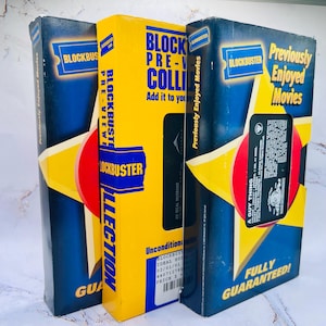 May include: Three vintage Blockbuster movie rental boxes. The boxes are blue and yellow with the Blockbuster logo and text. The boxes have the text "Previously Enjoyed Movies" and "Fully Guaranteed!"