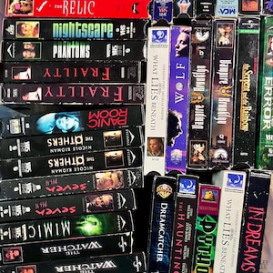 Może przedstawiać: Kolekcja kaset VHS ułożonych w siatkę, zawierająca tytuły takie jak The Relic, Nightscare, Phantoms, Frailty, Panic Room, The Others, Seven, Mimic, The Watcher, The Cell, What Lies Beneath, Wolf, Vampire in Brooklyn oraz In Dreams.
