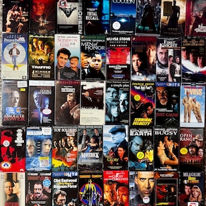 Peut inclure: Une collection de trente-cinq cassettes vidéo VHS disposées en grille. Les jaquettes présentent divers titres de films dont Bloodsport, Total Recall, The Matrix, Gladiator, Field of Dreams, Men of Honor, Twins et Dick Tracy, avec des étiquettes de prix.
