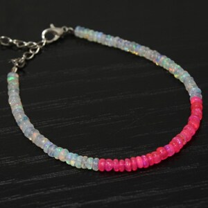 May include: A beaded bracelet with a colour gradient. The bracelet transitions from white and iridescent beads to a vibrant pink hue. It has a silver-coloured chain and clasp.