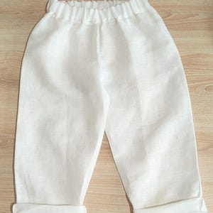 May include: White linen trousers with an elasticated waistband and turned-up hems. The trousers are made of a lightweight fabric. The garment is likely for children or babies.