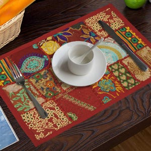 Könnte beinhalten: Ein roter Tischset mit einem Patchwork-Design mit Blumen- und Paisley-Mustern in verschiedenen Farben. Eine weiße Teetasse, Untertasse, Gabel und Messer sind auf dem Tischset angeordnet.