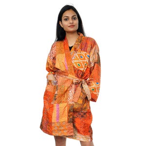 May include: An orange patchwork robe with long sleeves and a tie waist. The robe features a variety of orange, yellow, and pink fabric patches. The robe is knee-length and has pockets.