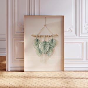 Könnte beinhalten: Ein gerahmter Aquarelldruck mit einem Makramee-Blatt-Design. Das Kunstwerk zeigt fünf hellgrüne Blätter, die an einem Holzdübel mit Naturgarn aufgehängt sind. Der Rahmen ist hellbraun und der Hintergrund ist ein neutrales Beige.