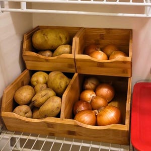 May include: Wooden storage bins filled with potatoes and onions. The bins are stacked on a wire shelf, with additional food items visible on the shelf above. The potatoes are a light brown color, and the onions are a golden brown.
