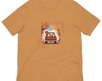 Könnte beinhalten: Senffarbenes T-Shirt mit einer Grafik von zwei Eichhörnchen in einer Ladefläche mit Kürbissen und Herbstlaub. Der Text "hello FALL" steht über dem LKW. Das Shirt besteht aus einem weichen Material.