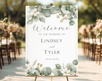 May include: A white wedding welcome sign with floral and eucalyptus accents. The sign reads "Welcome to the wedding of Lindsey and Tyler" with the date 03.06.20XX. The sign is displayed on a gold easel.
