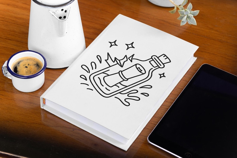 May include: A white notebook with a black line drawing of a message in a bottle. A small white mug with a blue rim and handle holds coffee. A white kettle and a tablet are also on the wooden surface.