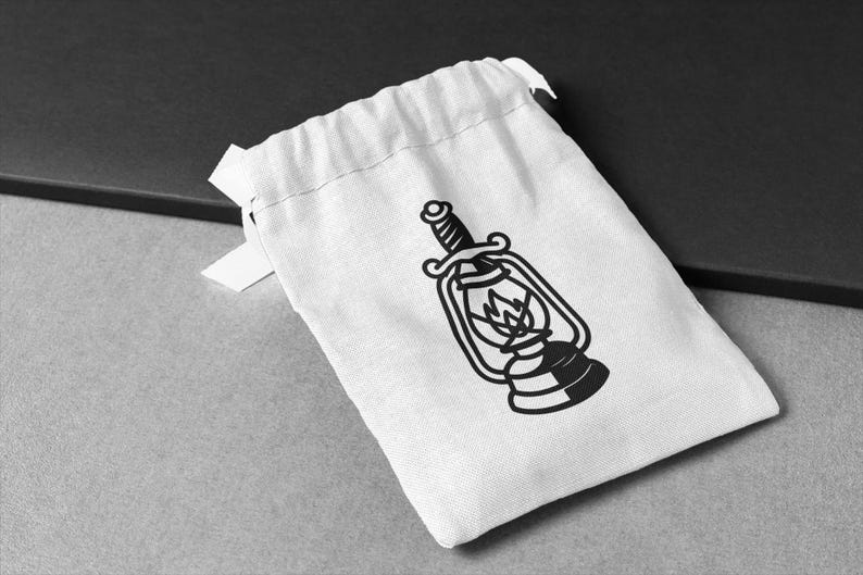 May include: A white drawstring bag with a black graphic of a vintage lantern with a sword through it. The lantern has a flame inside. The bag is on a gray surface.
