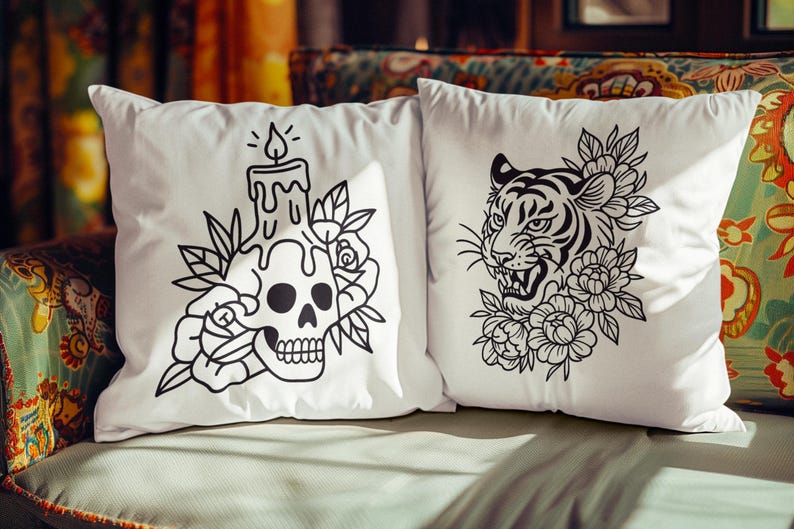 May include: Two white throw pillows with black graphic designs. One features a skull with a candle and floral accents, the other a tiger's face surrounded by flowers. The pillows are on a patterned sofa.