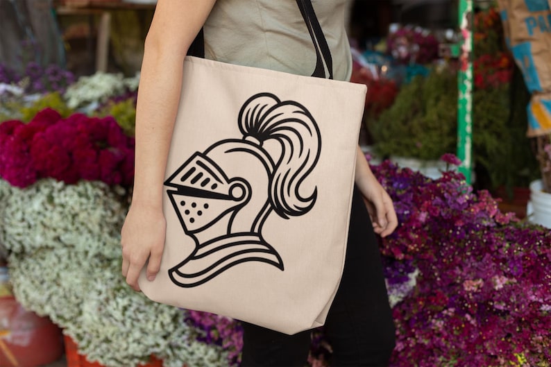 May include: Beige tote bag featuring a black line drawing of a knight's helmet with a visor and a flowing plume. The bag is carried by a person. The background includes colorful flowers.
