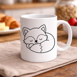 Puede incluir: Taza de cer&aacute;mica blanca con una ilustraci&oacute;n en contorno negro de un zorro durmiendo. El zorro est&aacute; acurrucado con los ojos cerrados. La taza tiene un asa curva y est&aacute; sobre una servilleta de lino beige.