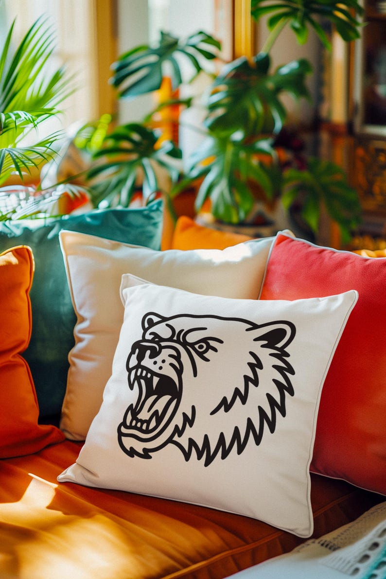 May include: A decorative pillow with a cream-colored background features a black illustration of a bear's head with an open mouth. The pillow is part of a collection of colorful pillows in shades of orange, teal, and red.