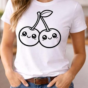 Puede incluir: Camiseta blanca con un dise&ntilde;o de cerezas de dibujos animados en blanco y negro. Las cerezas tienen caras sonrientes y est&aacute;n conectadas por tallos y una hoja. La camiseta se combina con vaqueros azules y un cintur&oacute;n marr&oacute;n.