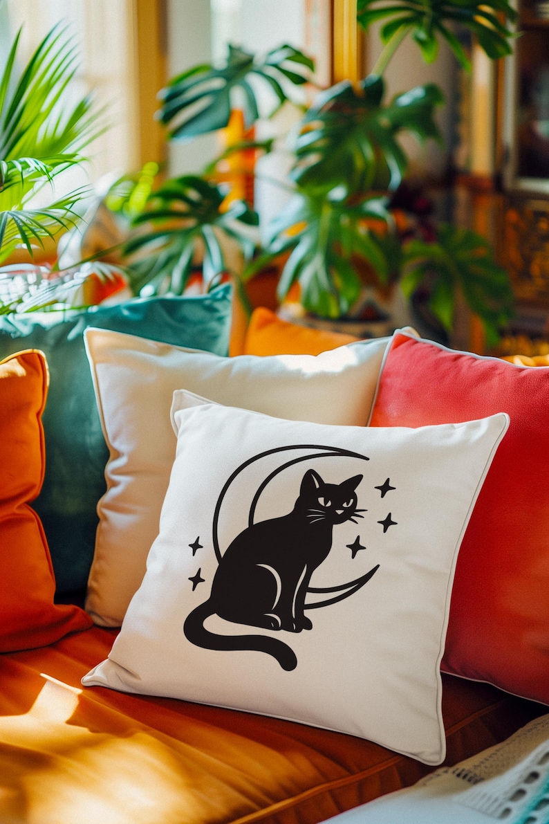 May include: A decorative pillow with a black cat silhouette sitting on a crescent moon, surrounded by four stars. The pillow is white and rests among other colorful pillows in shades of orange, teal, and red.