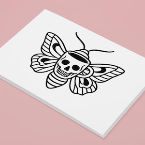 May include: A white card featuring a black illustration of a moth with a skull design. The moth's wings and body are detailed with black lines, creating a striking contrast against the white background. The card is set against a pink backdrop.