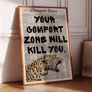 May include: A framed print featuring a newspaper background with the headline "New York Times" and the text "YOUR COMFORT ZONE WILL KILL YOU." A leopard with its mouth open is at the bottom of the print. The frame is brown.