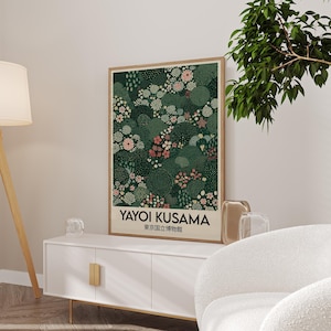 May include: A framed art print featuring a floral design in shades of green, pink, and white. The print includes the text "YAYOI KUSAMA" and Japanese characters. The artwork is displayed on a white cabinet with gold handles.