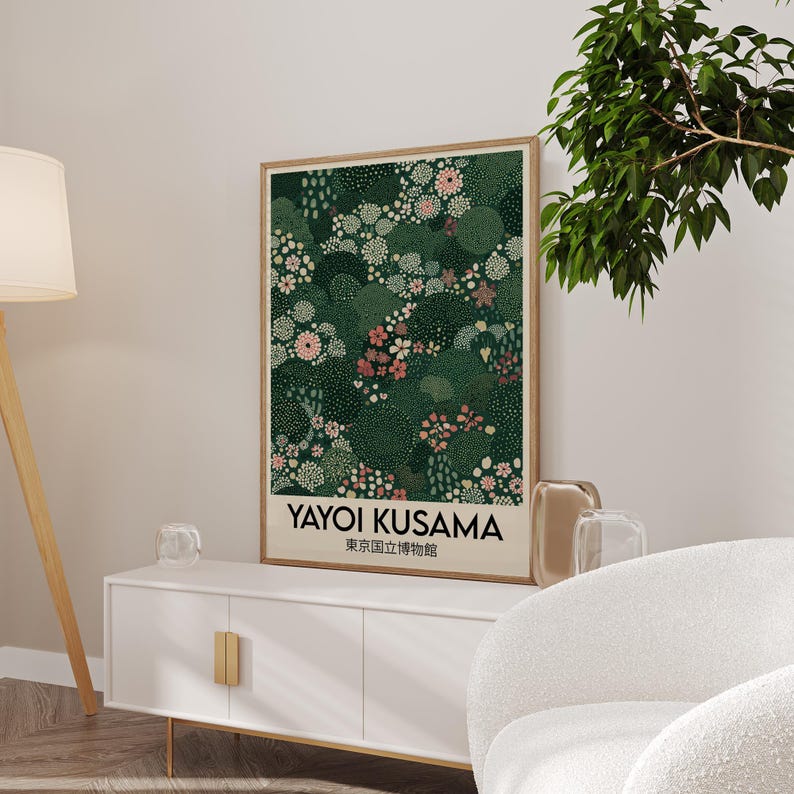 May include: A framed art print featuring a floral design in shades of green, pink, and white. The print includes the text "YAYOI KUSAMA" and Japanese characters. The artwork is displayed on a white cabinet with gold handles.