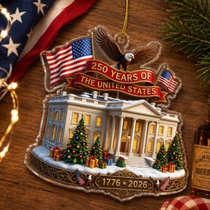 May include: A clear acrylic Christmas ornament depicting the White House, American flags, and an eagle. The ornament celebrates "250 YEARS OF THE UNITED STATES" with the years "1776 * 2026". Decorated Christmas trees and wrapped gifts are also visible.