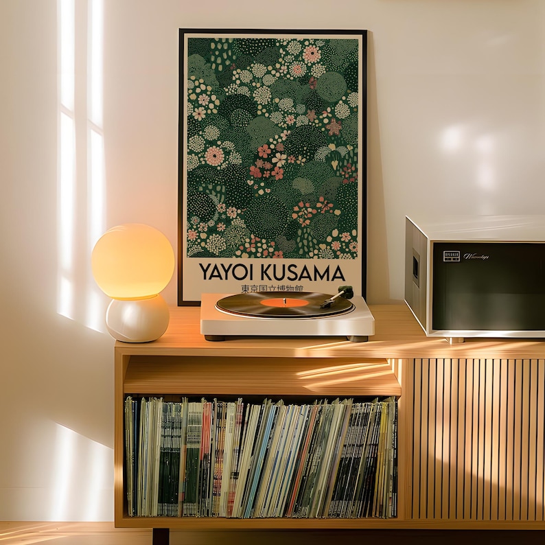 May include: A wooden cabinet with a collection of vinyl records, a white record player, and a framed poster featuring a floral design. The poster reads "Yayoi Kusama" and includes Japanese text. A white and yellow globe lamp sits on the cabinet.