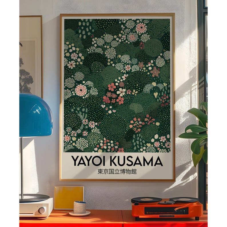 May include: A framed art print featuring a dark green floral pattern with white and pink flowers. The print includes the text "YAYOI KUSAMA" and Japanese text. The artwork is displayed in a room with a blue lamp and a record player.