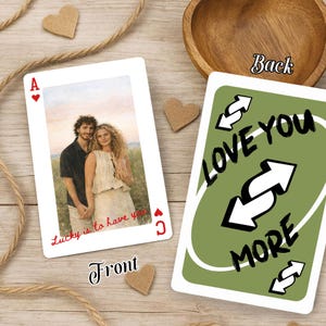 Puede incluir: Carta de juego personalizada con foto de pareja, texto "Lucky is to have you" y símbolo de As de corazones. El reverso muestra "Love You More" con flechas invertidas sobre fondo verde. También hay corazones decorativos y cuerda.