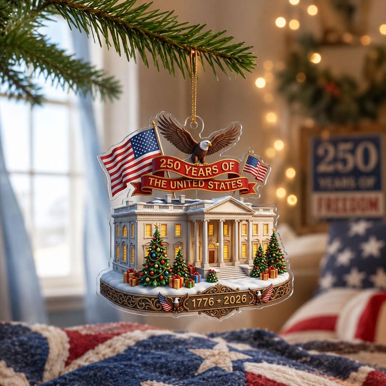 May include: A clear acrylic Christmas tree decoration depicting the White House, American flags, and an eagle. The ornament celebrates "250 Years of The United States" with the years 1776-2026. Christmas trees and gifts are also included in the design.