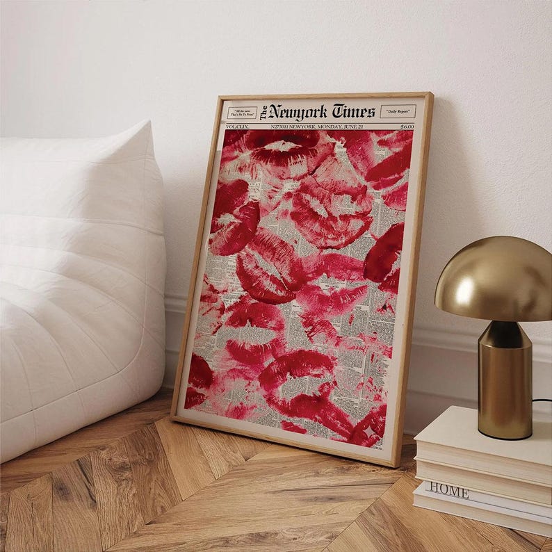 Pu&ograve; includere: Una stampa incorniciata con un collage di segni di baci di rossetto rosso su uno sfondo di giornale. La stampa &egrave; in una cornice di legno chiaro e include il testo "New York Times". Una lampada dorata e dei libri sono sullo sfondo.