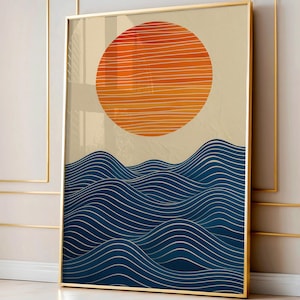 May include: Framed art print featuring an abstract landscape. The artwork depicts a large orange sun with horizontal lines above blue wavy lines, resembling ocean waves. The background is a light beige color, and the frame is gold.
