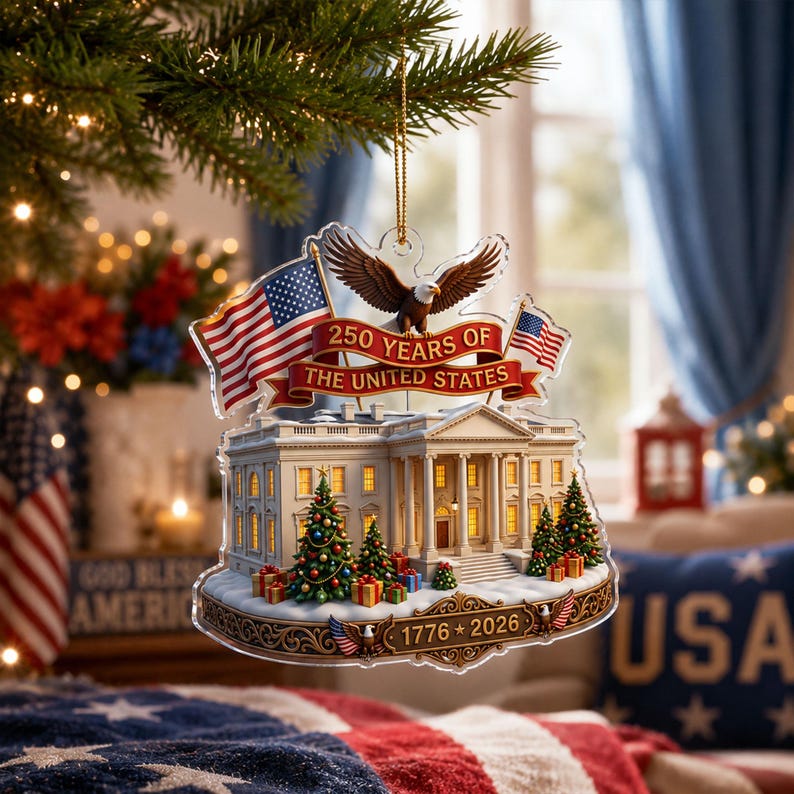 May include: A clear acrylic Christmas decoration depicting the White House, American flags, and an eagle. The ornament celebrates "250 YEARS OF THE UNITED STATES" with the years "1776 * 2026" displayed. The decoration is suspended from a Christmas tree branch.